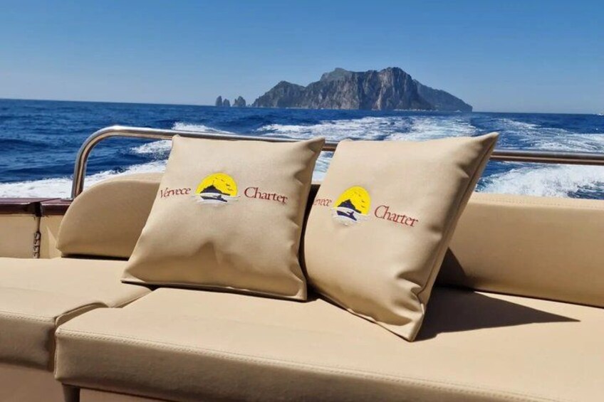 Una barca con cuscini beige e un logo, con un'isola rocciosa sullo sfondo. 5