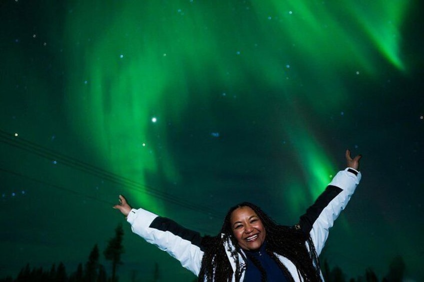 Una persona con le braccia alzate sotto un cielo notturno con aurore boreali verdi. 2
