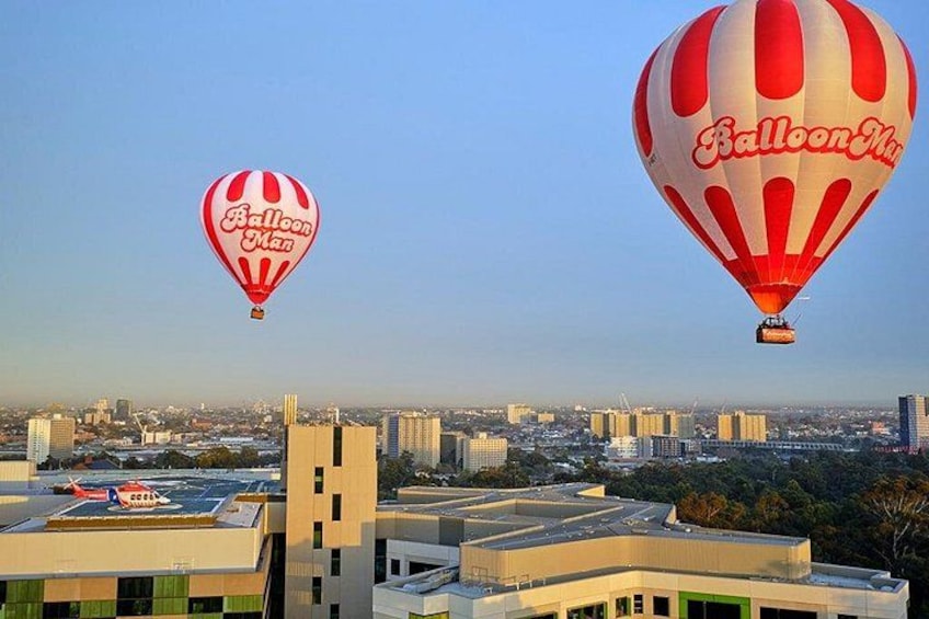 Due mongolfiere con la scritta 'Balloon Man' che sorvolano una città con edifici moderni. 2