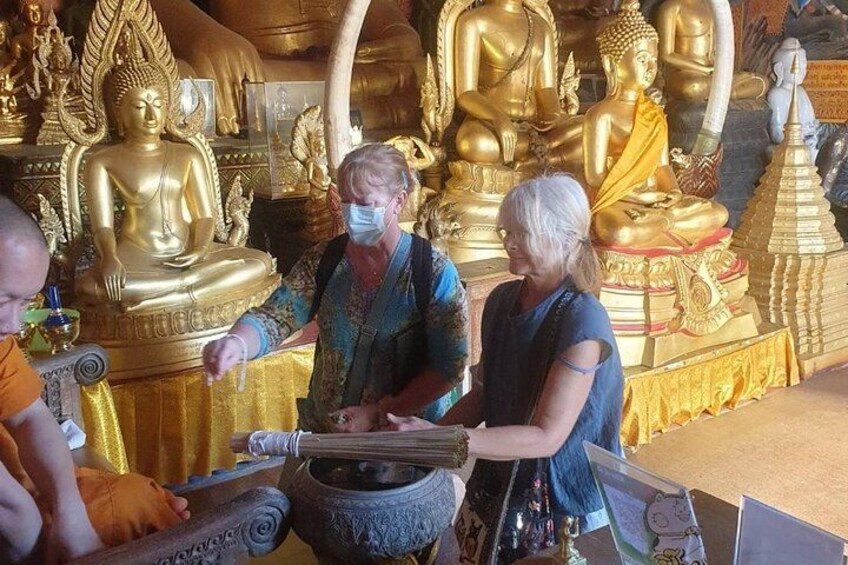 A person performing a ritual with a bowl and incense sticks in front of golden Buddha statues. 5