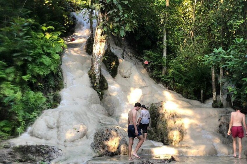 A waterfall in a forested area with people standing near the water. 1
