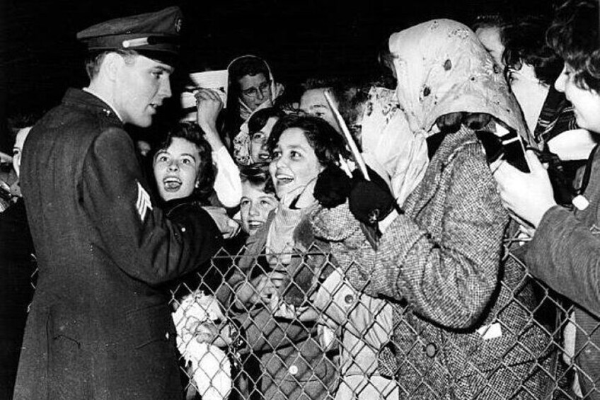 A military officer interacting with a crowd behind a chain-link fence. 2