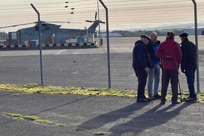 A group of people standing near a fence with a helicopter in the background. 3