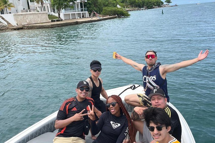 A group of people on a boat on a body of water with a dock and greenery in the background. 3