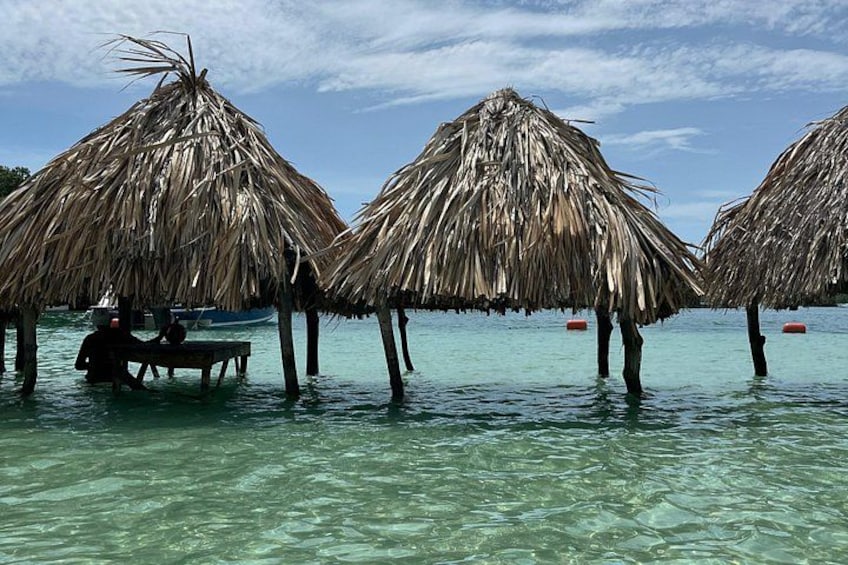 Thatched huts with a table and chairs in shallow water. 5