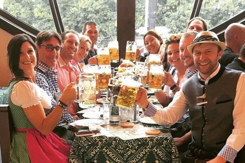 A group of people toasting with large beer mugs at a table with a patterned tablecloth. 3