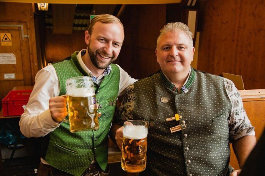 Two people holding large beer mugs in a wooden interior setting. 2