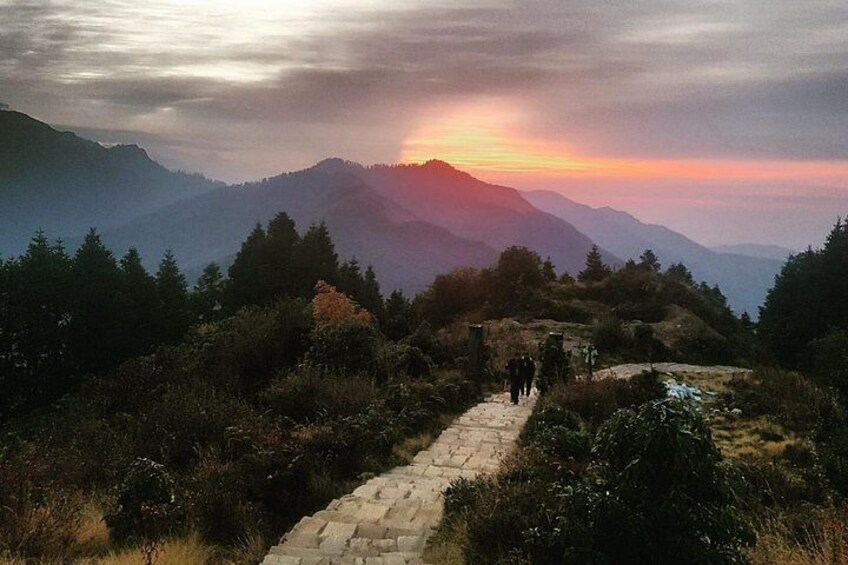 Un paysage montagneux avec un sentier de pierres, des arbres et un coucher de soleil. 4