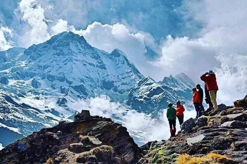 Un groupe de personnes se trouve au sommet d’une montagne rocheuse, avec une montagne enneigée en arrière-plan. 5