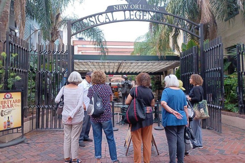 Un grupo de personas de pie en la entrada de un edificio con un letrero que dice 'New Orleans Musical College'. 2