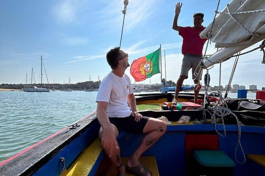 Una persona en un bote con una bandera, otra persona de pie en la cubierta y un paisaje urbano al fondo. 2