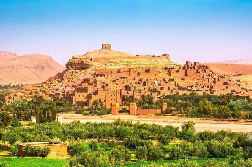 A traditional village with adobe buildings, a prominent hilltop structure, and surrounding greenery. 2