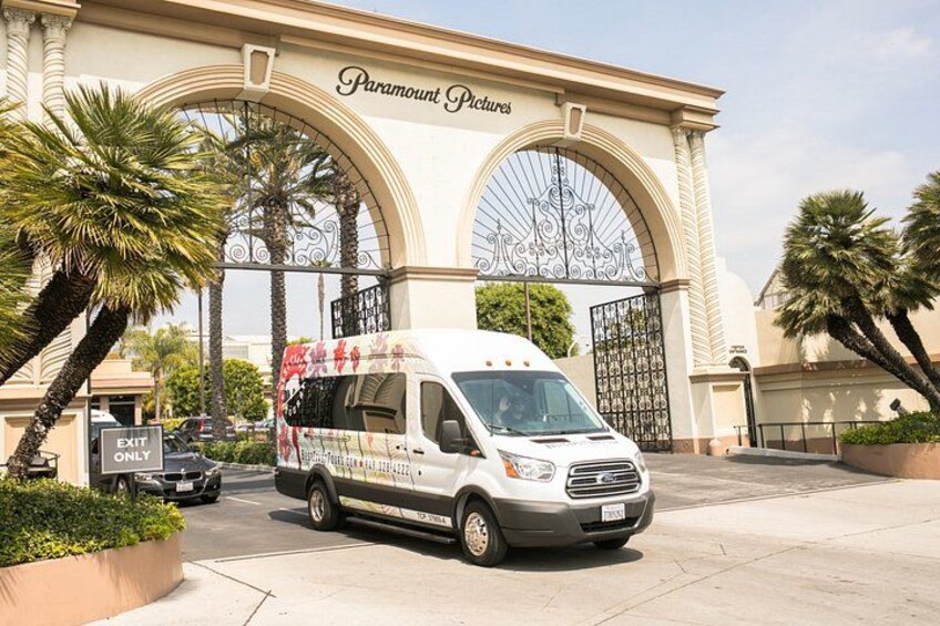 Una camioneta blanca estacionada frente a Paramount Pictures, con palmeras y una entrada protegida por una reja. 5