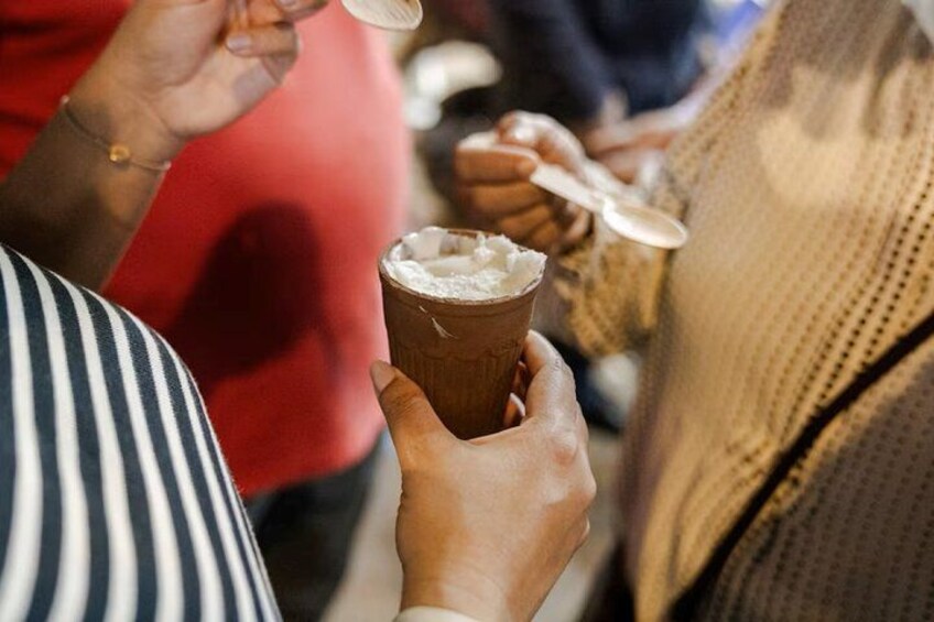 A person holding a cup with a white substance, possibly a dessert or drink, in a crowded setting. 5