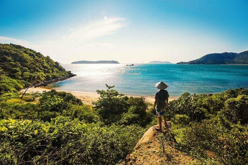 A person standing on a rock overlooking a beach with clear blue water and distant islands. 5