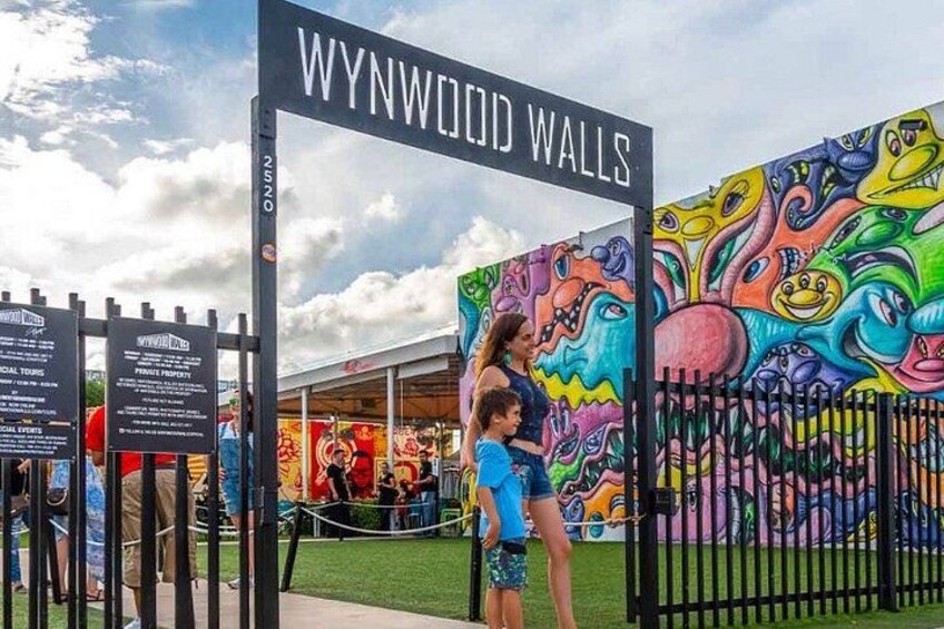 A colorful mural, a gate labeled 'WYNWOOD WALLS', and a person holding a child. 1