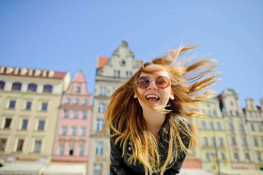Eine Person mit langem, wehendem Haar, im Hintergrund Gebäude unterschiedlicher Architektur. 1