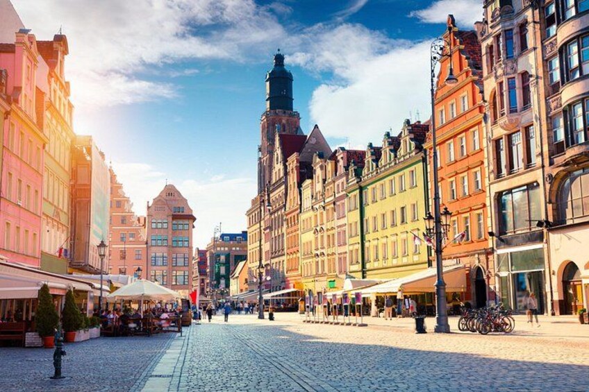 Ein Kopfsteinpflasterplatz mit historischen Gebäuden, einem markanten Turm und Straßencafés. 2