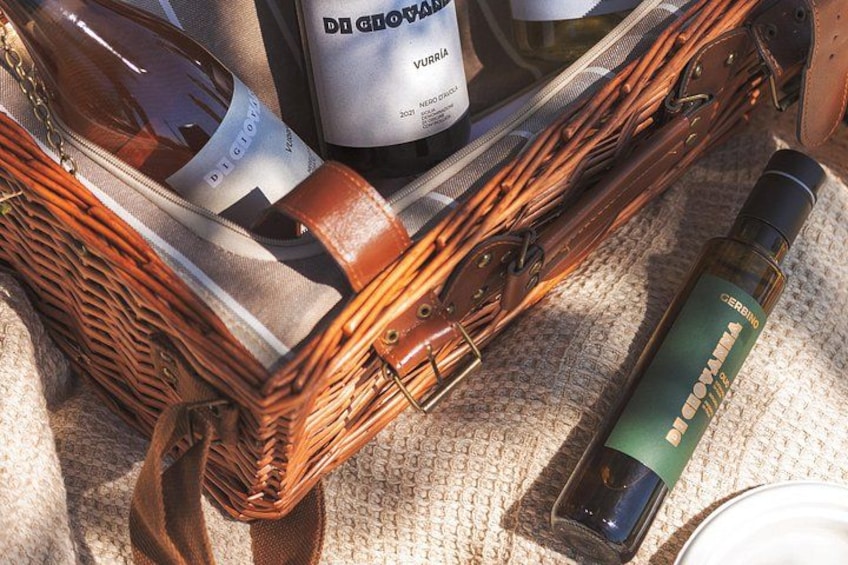 A wicker basket containing a bottle of wine, a bottle of sunscreen, and a bottle of olive oil. 4