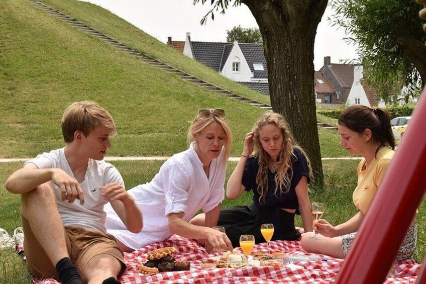 Ein Picknick mit Menschen, die unter einem Baum auf einer karierten Decke sitzen. 5