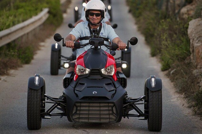 Eine Person fährt mit einem roten Quad auf einer schmalen Straße, gesäumt von Grünpflanzen. 2