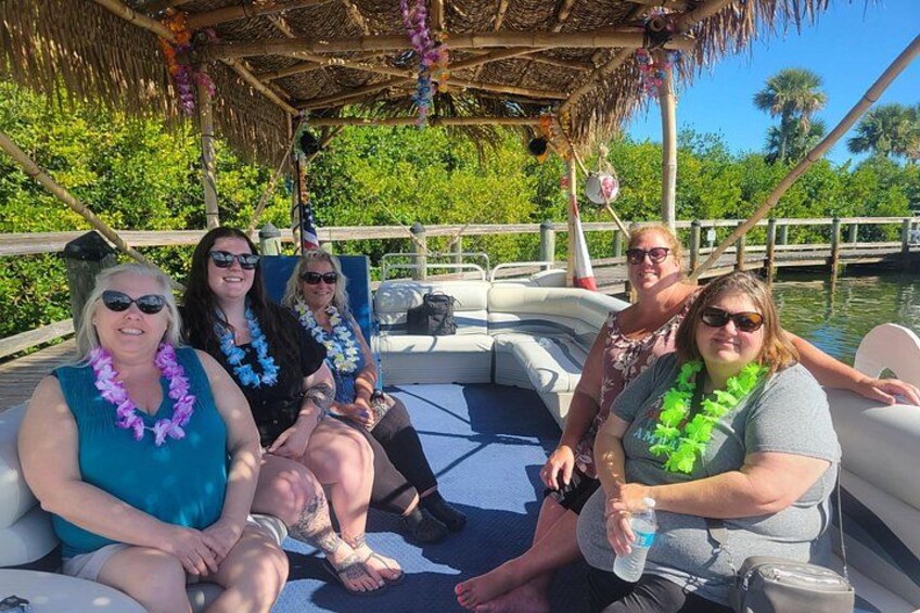A group of people on a boat with a thatched roof and palm trees in the background. 1