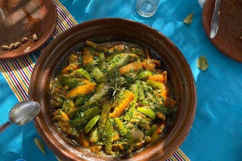 A traditional Moroccan tagine dish with vegetables and herbs, served in a clay pot on a blue cloth. 1