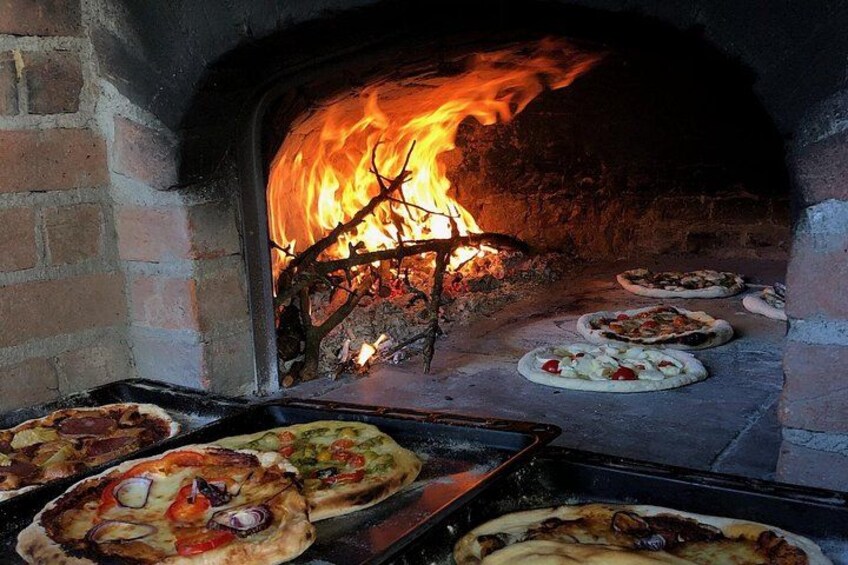 En murstensovn med pizzaer, der bages indeni, flammer synlige gennem brændkammeret. 3