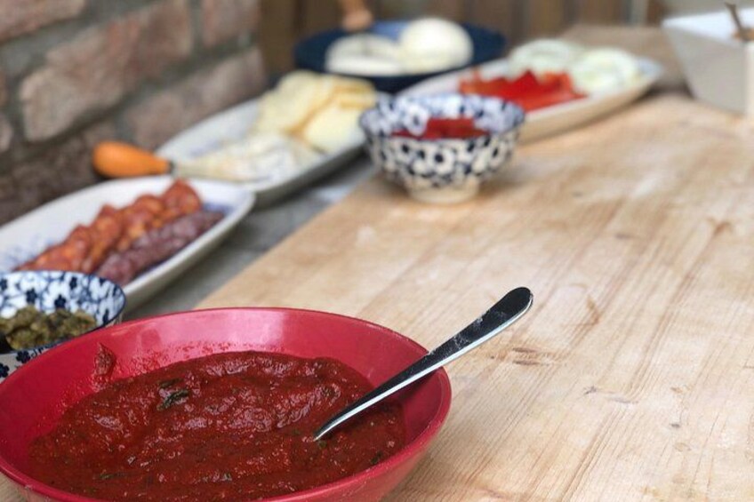 Una mesa de madera con diversos alimentos, incluyendo un tazón rojo con una cuchara, y platos con diferentes guisos al fondo. 2