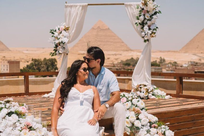 A couple seated at a wooden deck with a backdrop of pyramids. 1