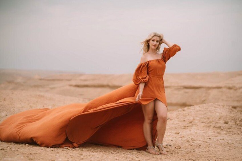 A person in an orange dress on a sandy beach with a desert landscape in the background. 5
