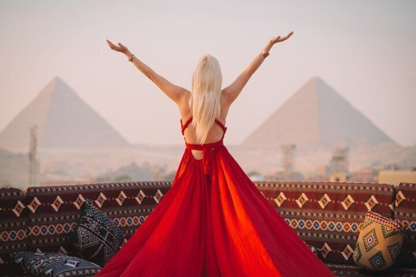 A person in a red dress with arms outstretched, facing the pyramids. 3