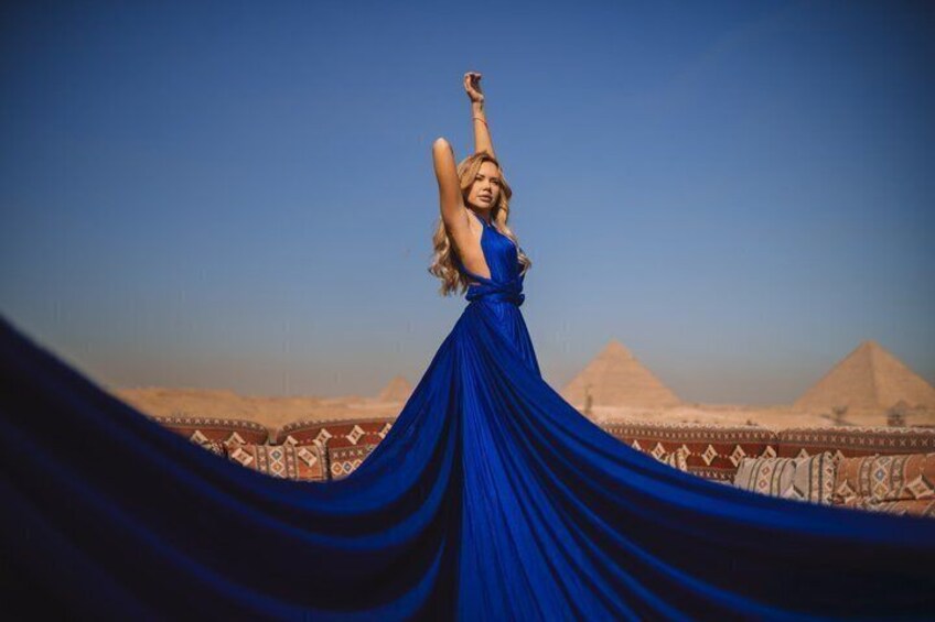 A person in a flowing blue dress with a desert landscape and pyramids in the background. 2