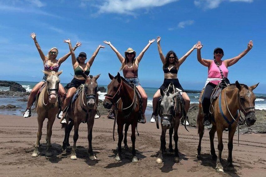 Four people riding horses on a beach with the ocean in the background. 1