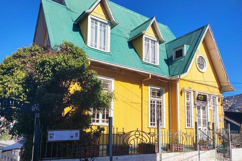 A yellow house with a green roof, white windows, and a metal fence. 3