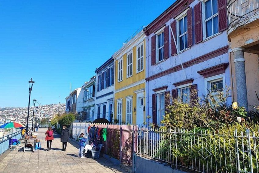 A waterfront promenade with colorful buildings, a fence, and a clear blue sky. 2