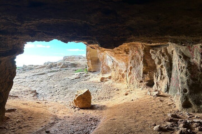 A cave entrance with a large rock in the foreground and a view of the outside landscape. 2