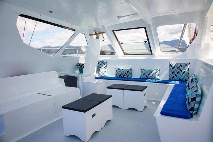 A boat interior with a white and blue color scheme, featuring a seating area with cushions, a table, and a window. 3
