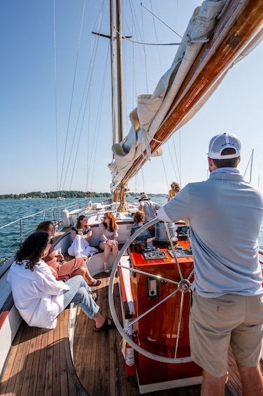 A group of people on a sailboat with a man steering. 1