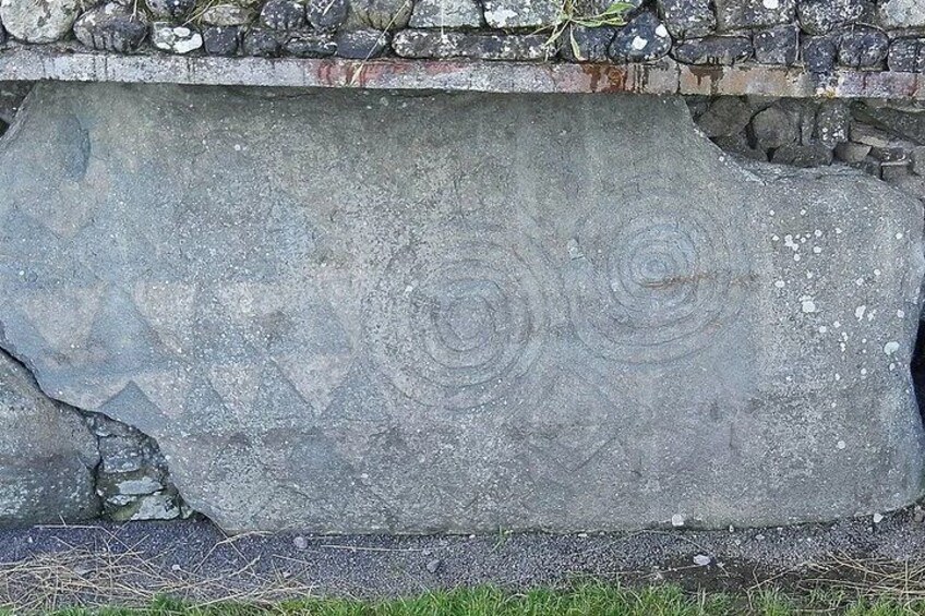A weathered stone with circular carvings and a crack running through it. 1