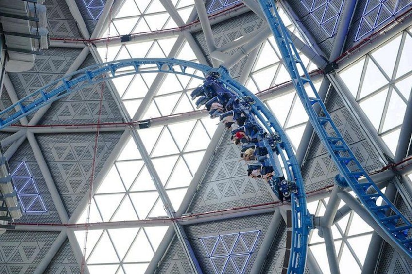 Una montaña rusa en un parque temático interior grande, con una estructura metálica geométrica y paneles de vidrio. 3