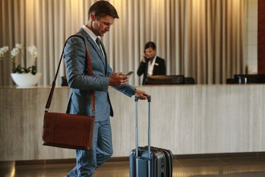 A man in a suit with a brown shoulder bag and a rolling suitcase in a hotel lobby. 5