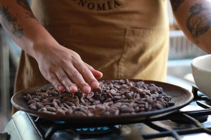 A person in an apron handling coffee beans on a stove. 3