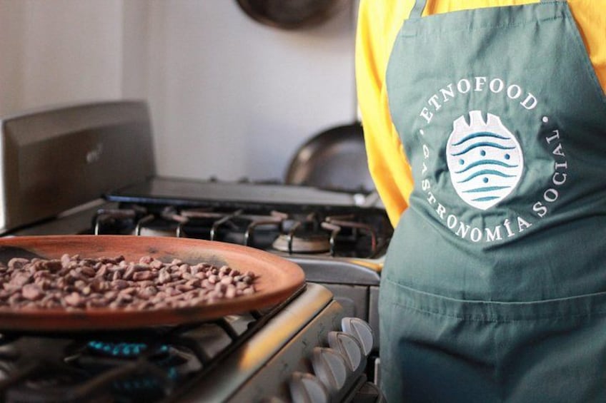 A person wearing a green apron with a logo, cooking on a stove with a pan of food. 4