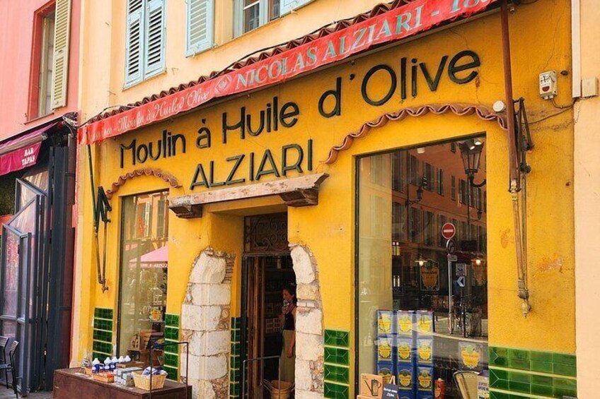 Fachada amarilla con un letrero que dice 'Moulin à Huile d'Olive ALZIARI' y una exhibición de botellas de aceite de oliva. 5