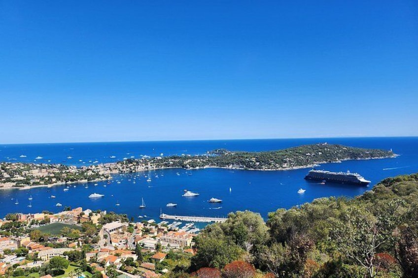 Un pueblo costero con un crucero grande atracado, numerosos barcos y un cielo azul despejado. 1