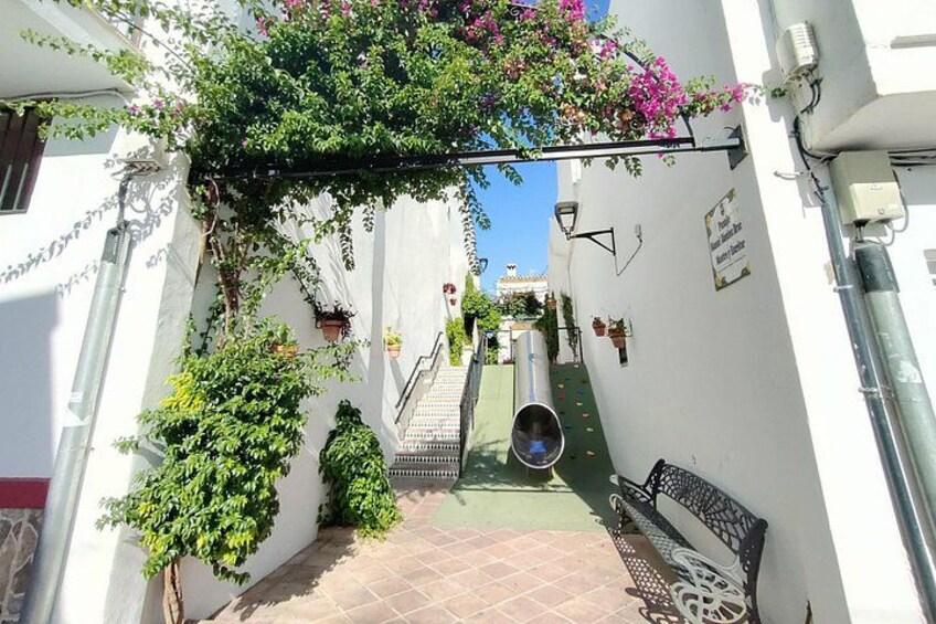 A narrow alleyway with a bench, a staircase, and potted plants. 4
