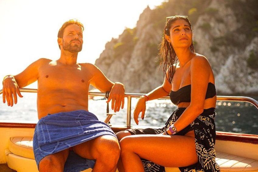 A man and a woman on a boat with a rocky coastline in the background. 3