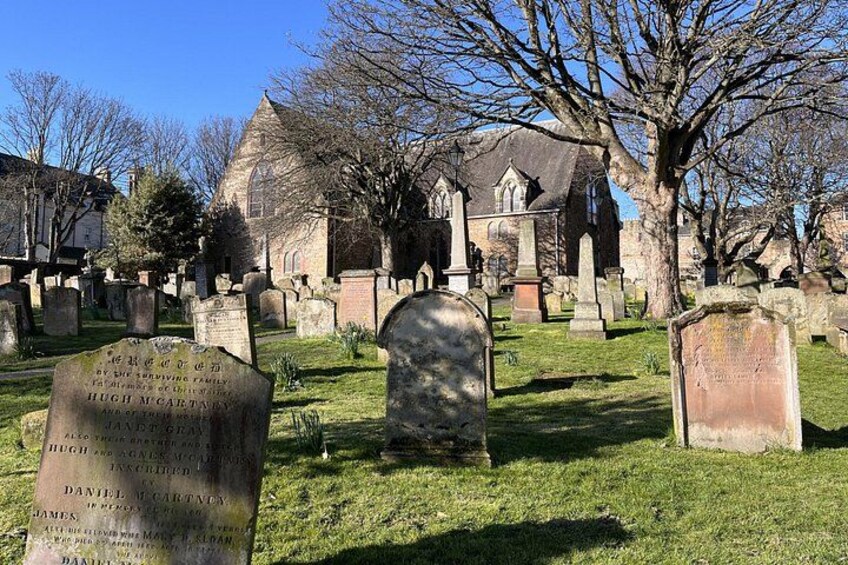 A cemetery with headstones, a church, and leafless trees. 4