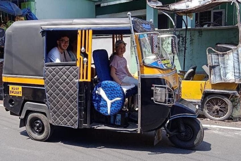 A tuk-tuk with two passengers, a man and a woman, on a street. 1